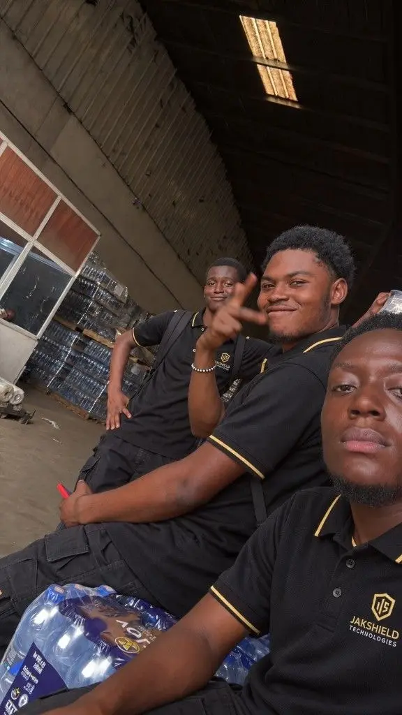 Three JakShield installers in black-and-gold JakShield uniforms taking a selfie during a break at a warehouse job.
