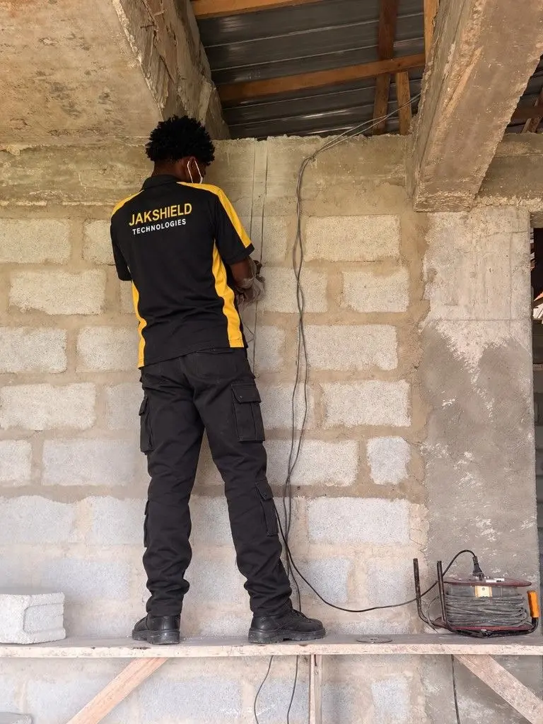 A JakShield technician in uniform routing cables along a block wall of a building under construction.